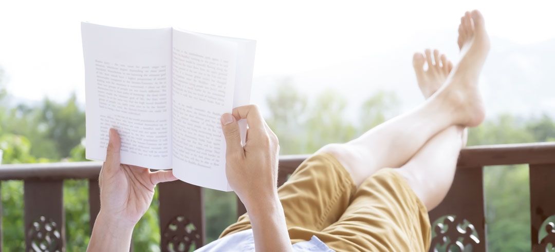 Persona leyendo en una terraza con los pies sobre una barandilla