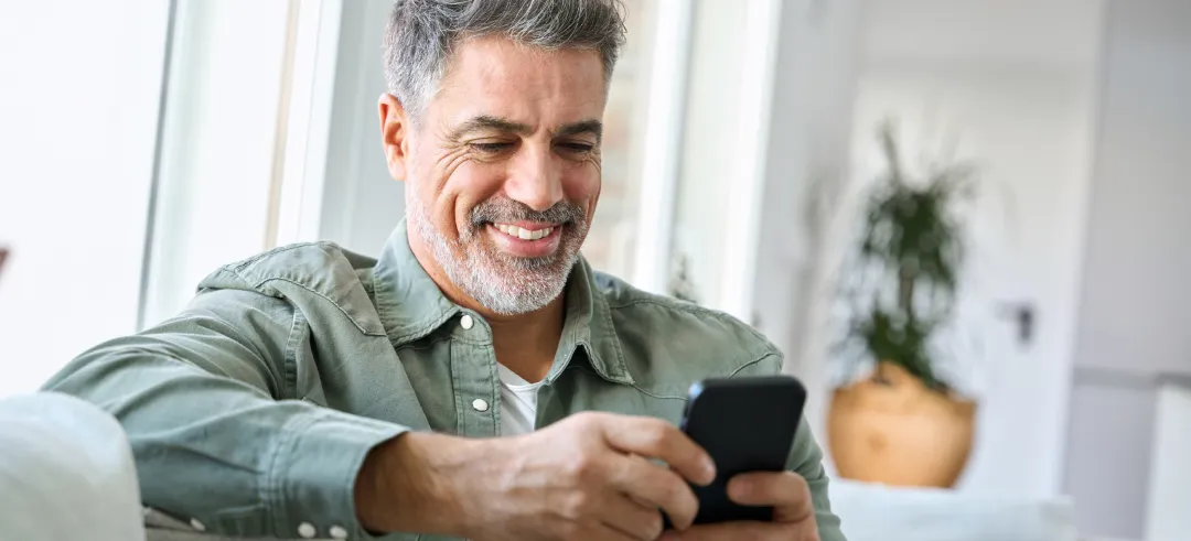 Hombre sentado en el sofá mientras utiliza su teléfono móvil